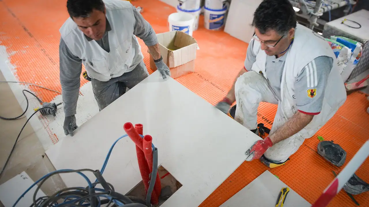 Dos profesionales colocan una baldosa cortada de gran formato sobre la lámina de desolidarización DITRA en la Torre Eiffel