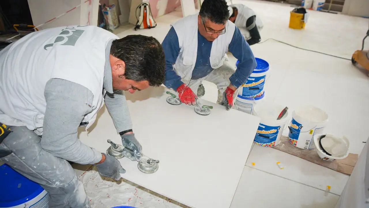 Dos profesionales colocan una baldosa de gran formato sobre la superficie de suelo preparada en la Torre Eiffel