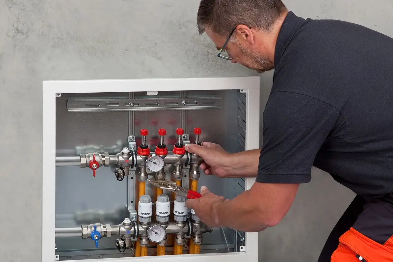Un profesional de Schlüter-Systems realiza ajustes en el distribuidor de una caldera para la calefacción por suelo radiante BEKOTEC-THERM.