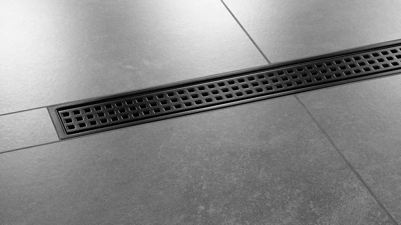 Primer plano de una ducha alicatada en gris oscuro con desagüe lineal Schlüter-KERDI-LINE-B en diseño SQUARE negro mate TRENDLINE instalada en el centro