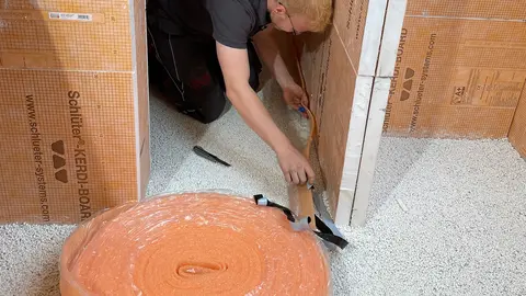 Un instalador coloca la cinta perimetral BEKOTEC-BRS, que sirve de transición entre el suelo y las paredes.