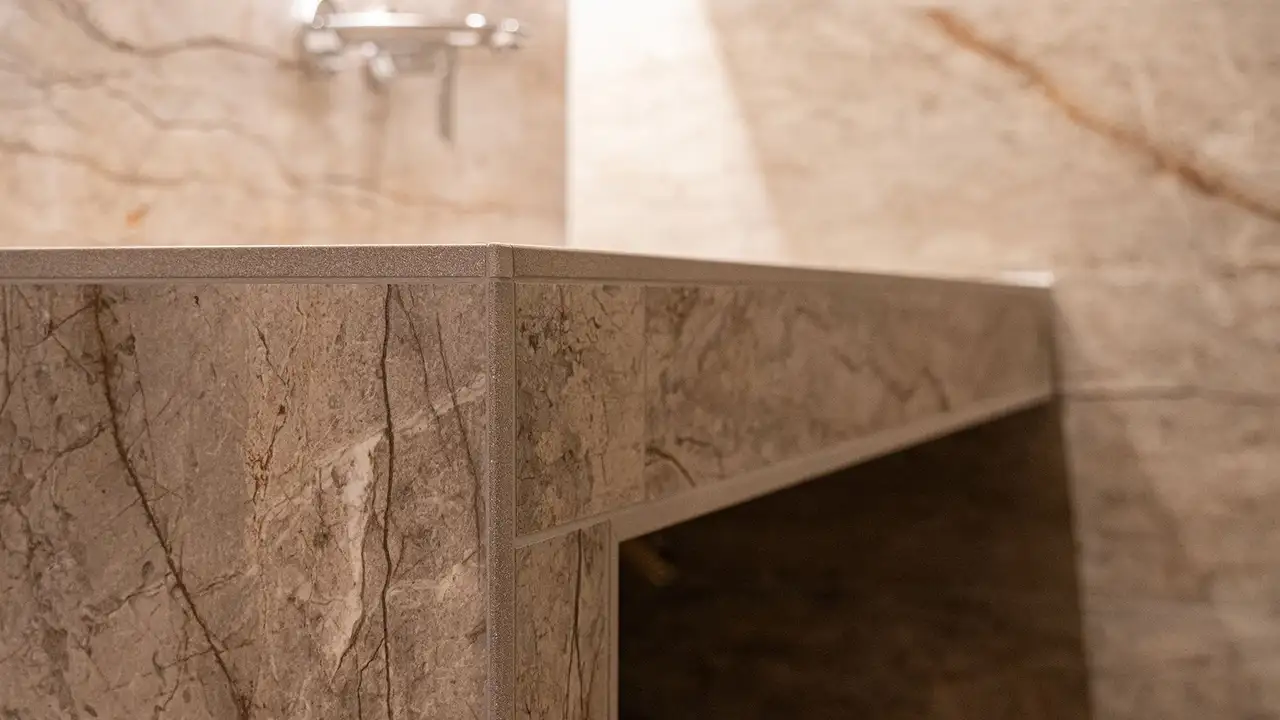 Gros plan sur le bord du lavabo doté d'un carrelage d'aspect marbre beige et un profilé de finition Schlüter-JOLLY assorti