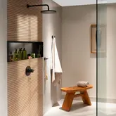 Douche ouverte avec paroi en verre, carrelage imitation bois et niche murale noire le long du mur arri&egrave;re