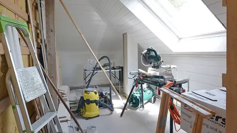 Vue de l'ancien atelier, avec toit mansardé, grande fenêtre et murs en bois clair.