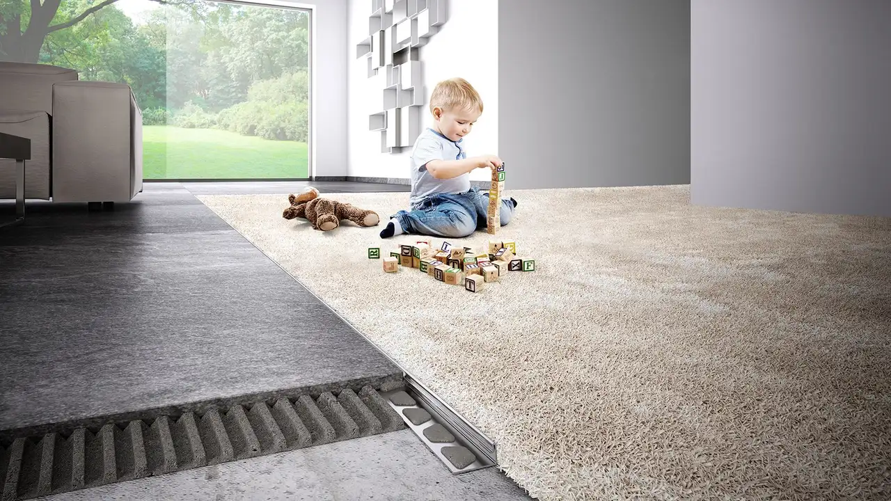 Un enfant joue avec des blocs de construction sur un tapis. Au premier plan figure une coupe de la structure du sol con&ccedil;ue avec des profil&eacute;s Schl&uuml;ter.