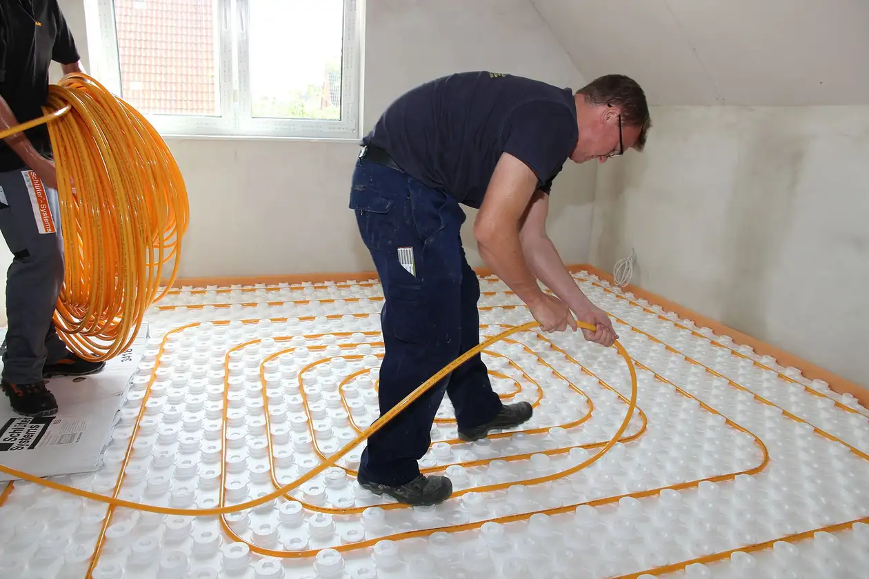 Un artisan clipse les tubes de chauffage sur une dalle à plots BEKOTEC à l'étage dans un bâtiment neuf