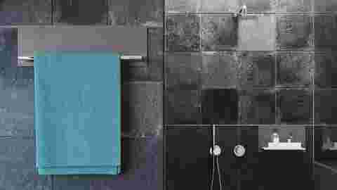 Une salle de bains avec revêtement carrelé de couleur sombre et porte-serviettes gris de la gamme Schlüter-ARCLINE.