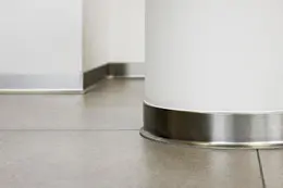 Sol avec plinthes en aluminium bross&eacute; autour d'une colonne blanche et le long d'un mur blanc