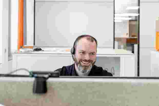Un collaborateur de Schlüter-Systems regarde l'écran de son PC en souriant.