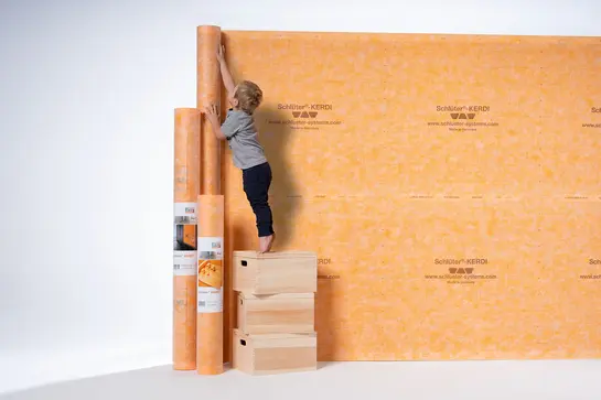 Un petit garçon regarde différents produits d’étanchéité Schlüter-KERDI.