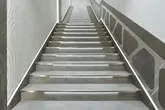 Escalier avec carrelage gris clair, applications murales et bandes lumineuses au-dessus des marches