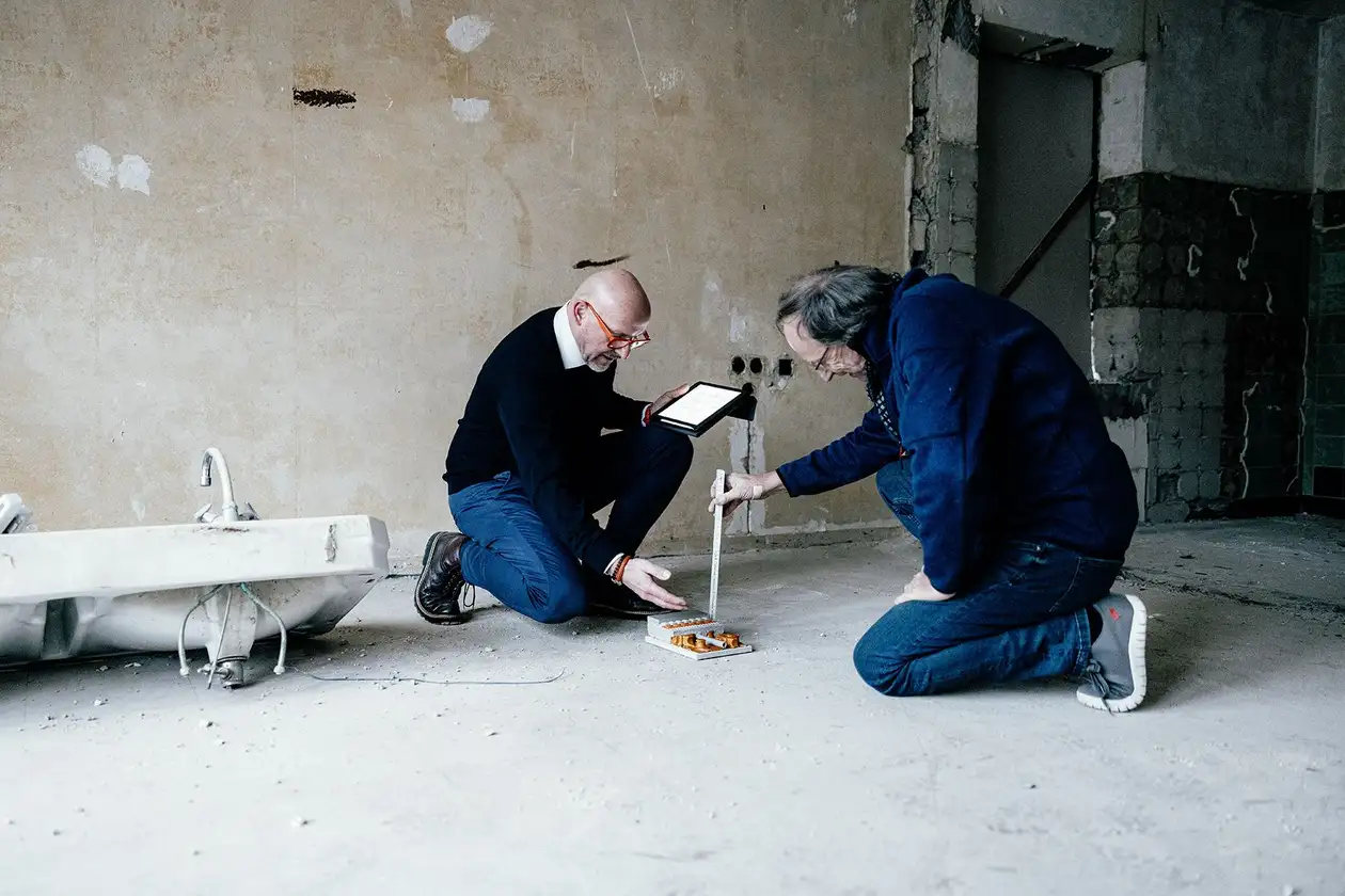 Deux maîtres d'œuvre mesurent la hauteur de montage approximative du plancher chauffant BEKOTEC-THERM sur un chantier dans un bâtiment en rénovation.