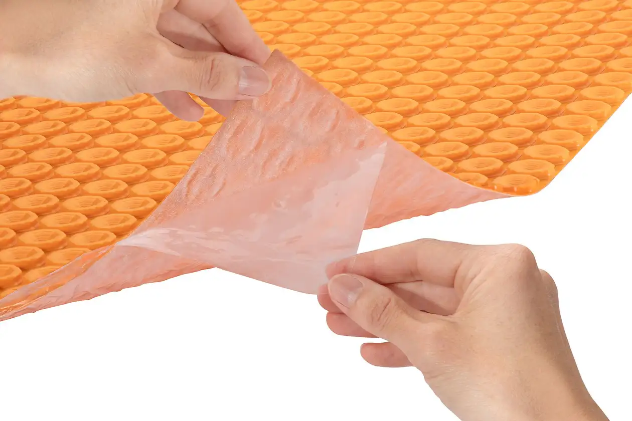 Natte autocollante Schlüter-DITRA-HEAT dont le film sur la face inférieure doit être retiré.