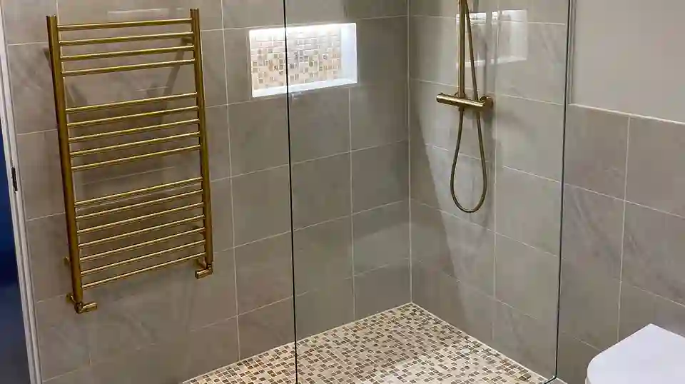 Douche à l'italienne avec sol en mosaïque, niche murale assortie, radiateurs et robinetterie de douche dorés.