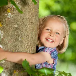 A little blonde girl hugging a tree.