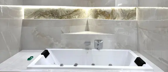 An illuminated bathtub in front of a curved wall with niches and light-grey, large tiles