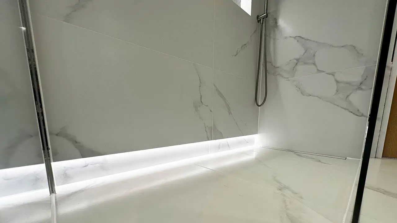 A close up of a shower area with indirect lighting at the bottom of the wall