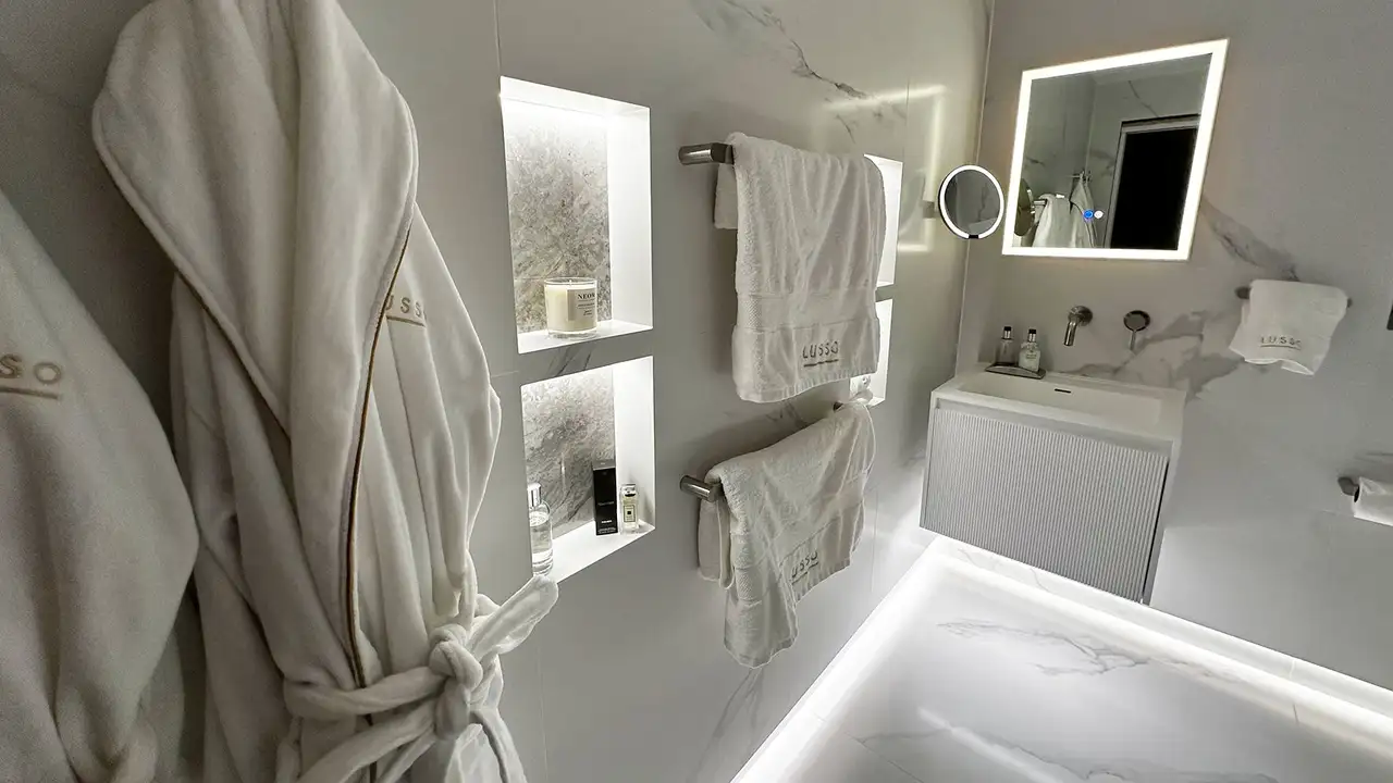 Bathroom corner with LED-lit wal niches, towels, robes, washbasin and mirrors
