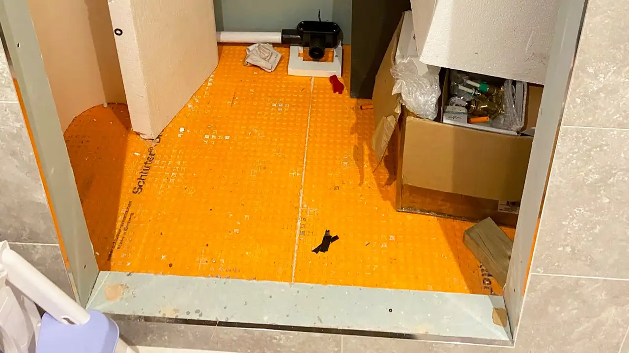Shower entrance with light grey tiles and orange Schlüter-DITRA mat on the shower floor