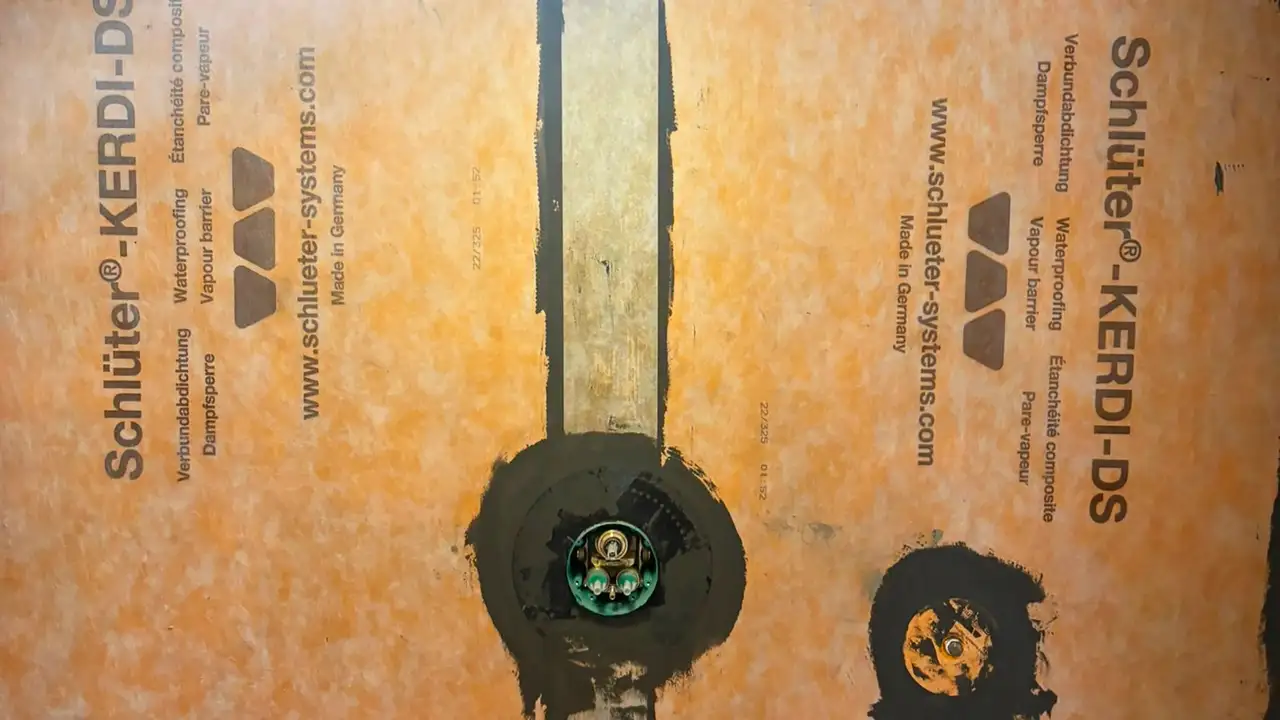 Shower wall with orange Schlüter-KERDI-DS installed and dark grey KERDI-COLL adhesive