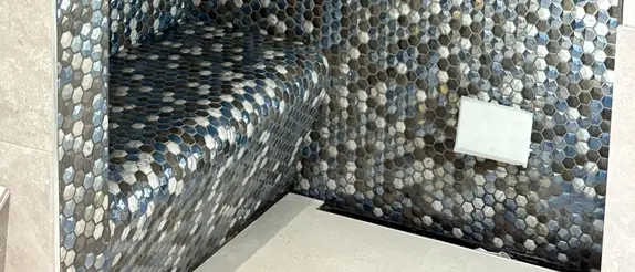 Bench tiled with greay, white and blue hexagon tiles in a shower