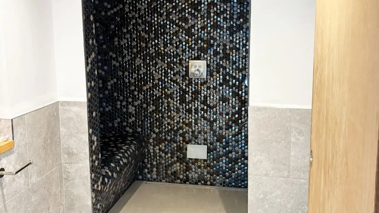 Shower entrance with small mosaik tiles and a bench on the left shower wall