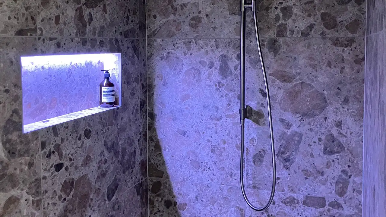 Close-up shot of a shower wall with large marble tiles and an illuminated niche