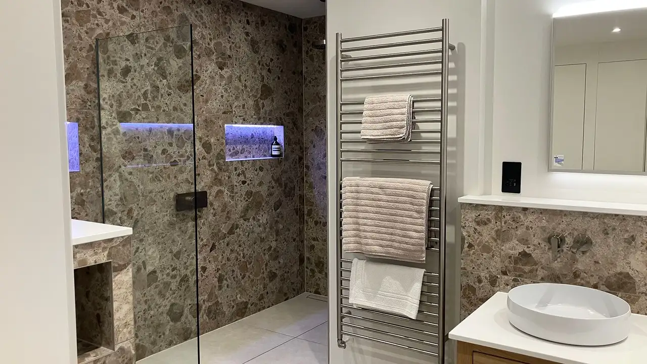 Finished renovated bathroom with large marble tiles, shower with illuminated niche and wash basin