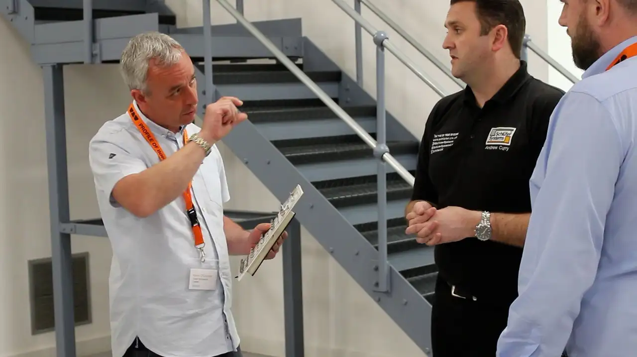 Three men pictured, one holding a sample of Schlüter product, are in discussion