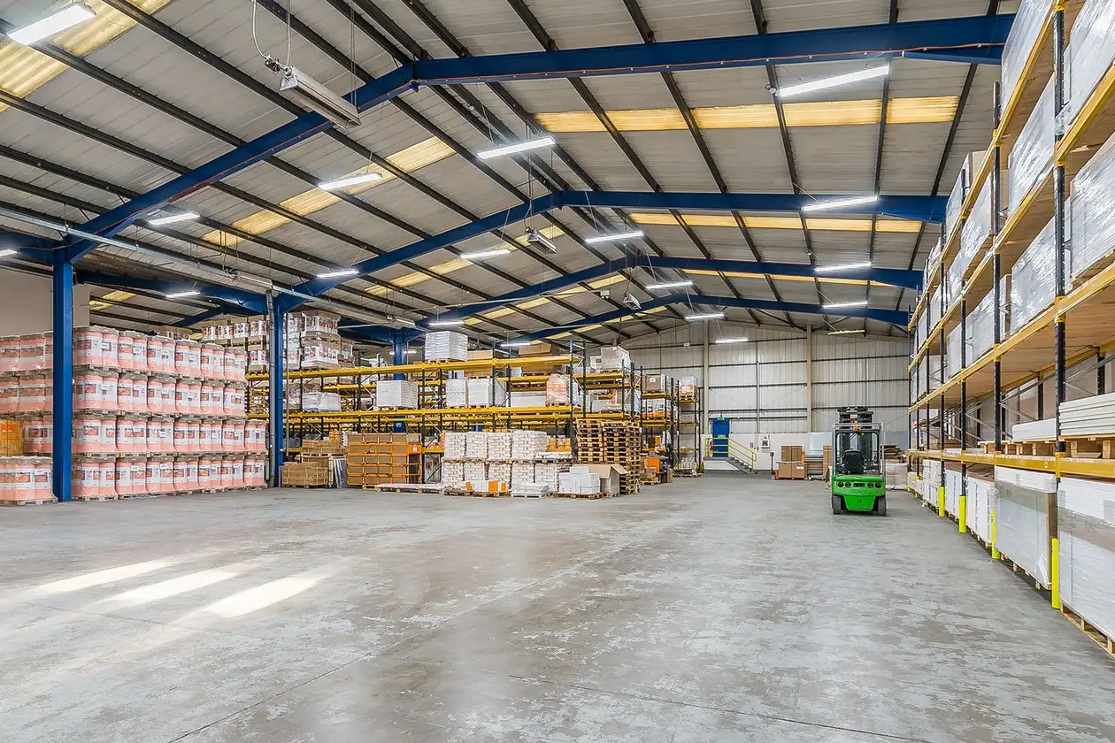 A wide angle shot of Schlüter's warehouse in the UK. Shelving full of product is in the far left corner and along the right hand side. A parked green forklift truck is next to the shelving