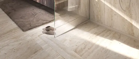 Beige tiled floor area of a level access shower with glass wall and KERDI-LINE-VARIO shower drainage channel