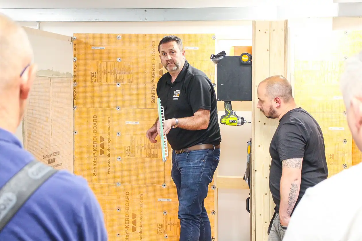 Two participants of a training course pictured intently listening to the Training Manager who is holding a tile profile