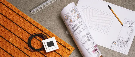 Ditra-Heat with thermostat and cable laid out on the floor, next to it are rolled and flat planning documents and a pencil. In the top left, a section of a Schl&uuml;ter-SCHIENE is visible.