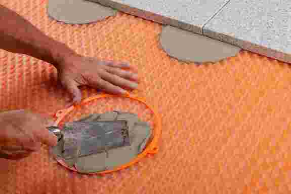 A formwork ring on a drainage mat is filled with mortar and placed so that it supports the corners of the pavers