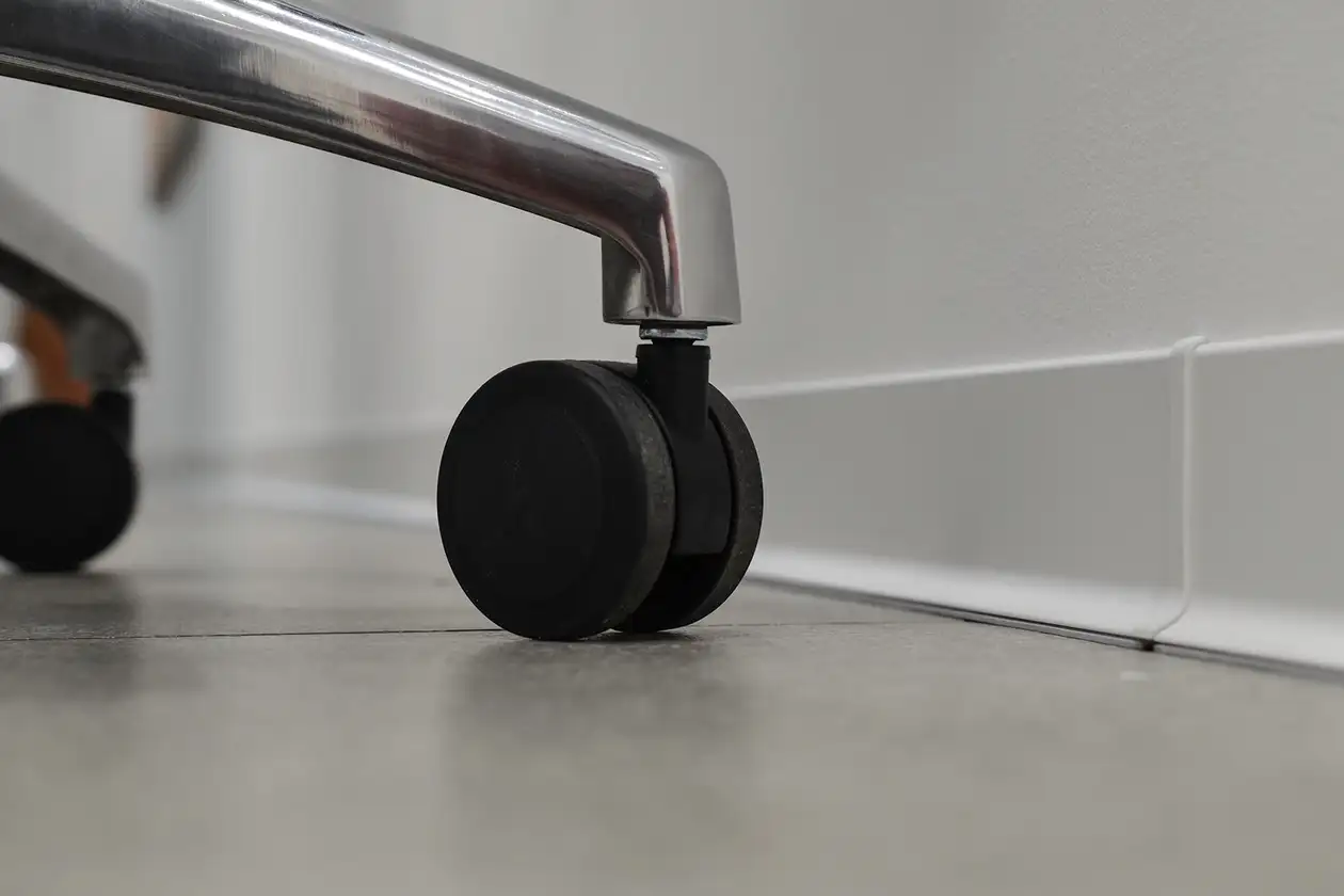 Close-up of the black wheels of an office chair in front of a white baseboard on a white wall