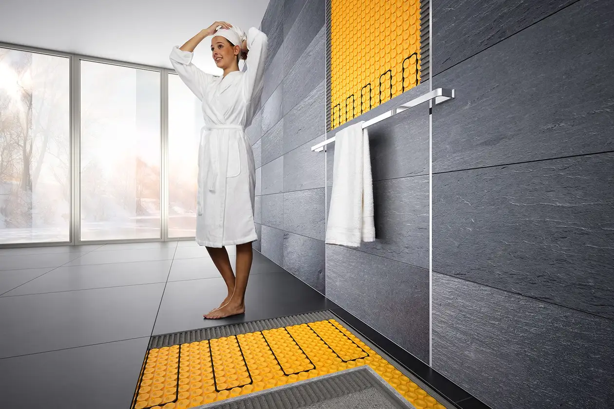 Young woman in the bathroom wearing her bathrobe, shower wall and floor are heated with DITRA-HEAT-E.