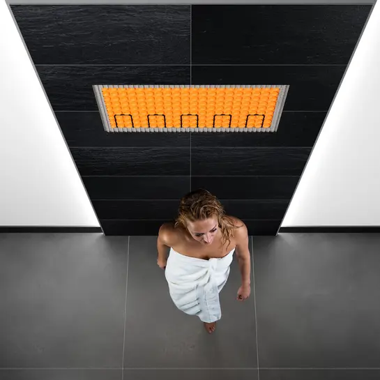 Woman in the bathroom standing in front of a wall surface heated with DITRA-HEAT-E.