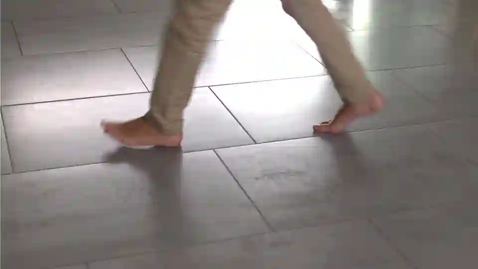 Man walking barefoot over tiles heated by the floor heating system.