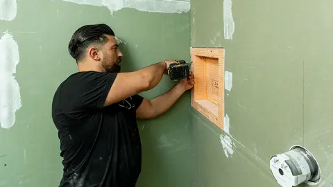 A contractor screws a niche made of orange KERDI-BOARD panels into a turquoise plasterboard wall