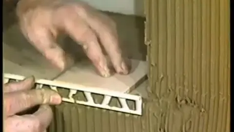 A 80-as évekből származó régi csempézési videóból kiragadott kép azt mutatja be, hogyan történik a Schlüter-SCHIENE csempe külső élén való elhelyezése