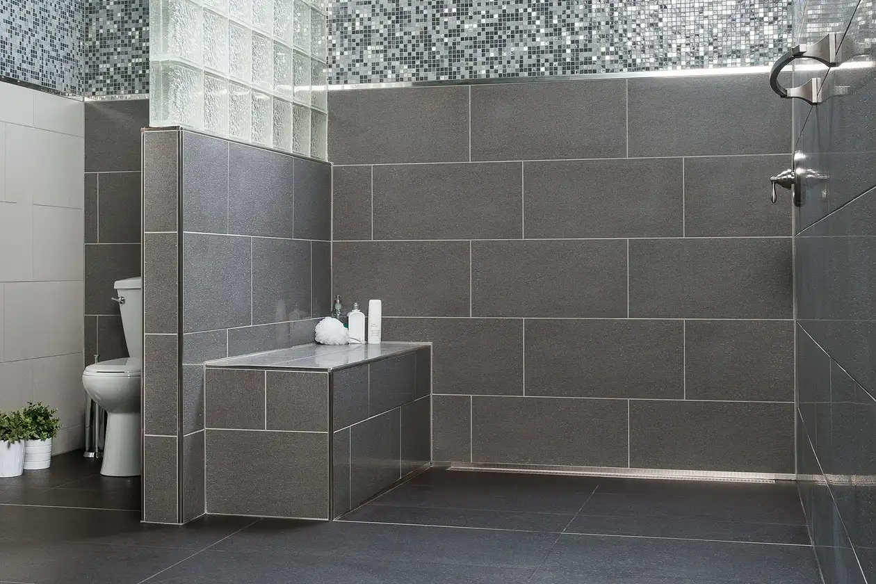 Bagno grigio, senza barriere architettoniche, con doccia a filo pavimento e panca per doccia con rivestimento in ceramica.