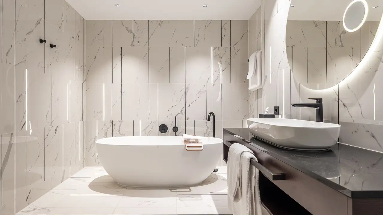 Ampio bagno d'albergo con piastrelle in marmo bianco, strisce luminose sulle pareti e vasca da bagno freestanding