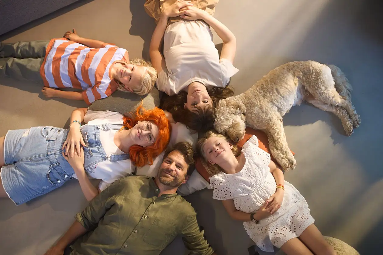 Una famiglia di cinque persone con un cane è seduta in cerchio su un pavimento ceramico piacevolmente fresco