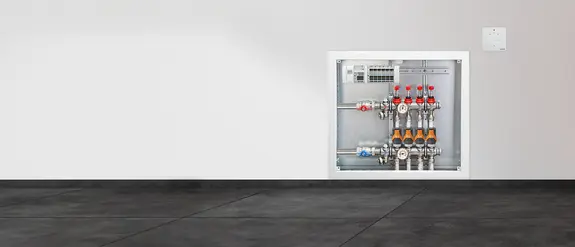 Collettore aperto di un sistema di riscaldamento a pavimento in una parete bianca su un rivestimento ceramico grigio scuro