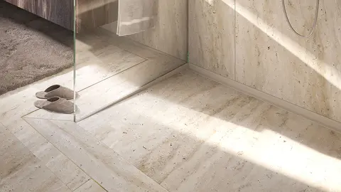 Beige betegelde vloer van een inloopdouche met glazen wand en KERDI-LINE-VARIO-WAVE douchegoot