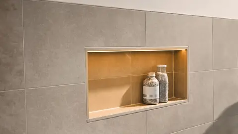 Verlichte nis in een lichtgrijs betegelde wand met twee flessen badzout