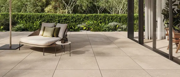 Terras met grote beige tegels, een stoel en een tafel voor een grote glazen deur.