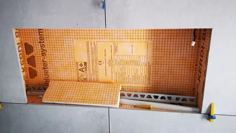 Aanzicht van een grijze tegelwand waarin de verlichte KERDI-BOARD-NLT-nis is ingebouwd.