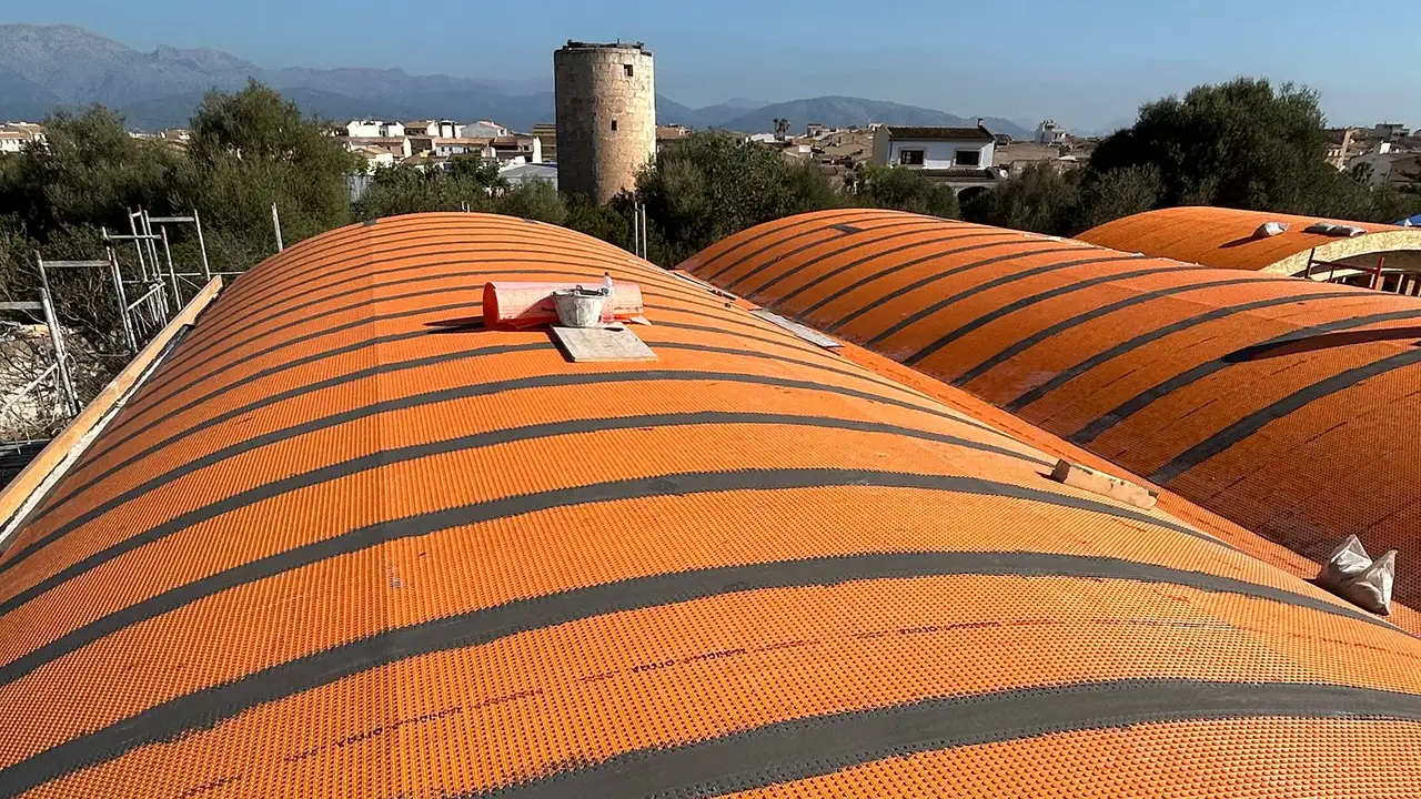 Dois trabalhadores instalam a membrana de desacoplamento laranja DITRA sobre os telhados curvos da creche em Muro