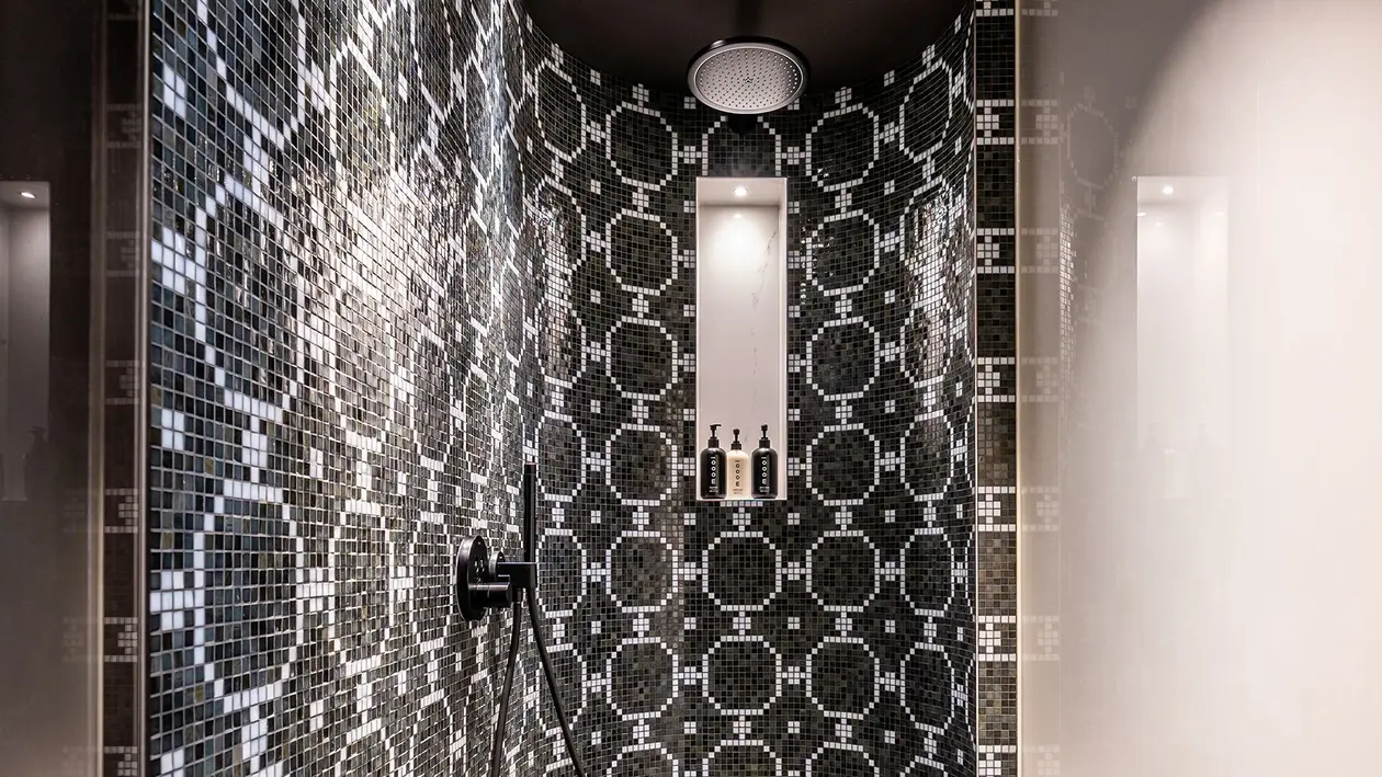 Chuveiro tipo cascata com parede traseira arredondada, nicho iluminado e azulejos ornamentais a preto e branco